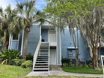 A charming blue two-story condo with a white staircase, surrounded by lush landscaping and mature trees at 2524 Grassy Point Dr # 104, Lake Mary, FL 32746