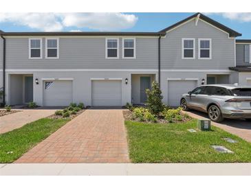 Charming townhome exterior with gray siding, brick driveway, and well-maintained landscaping at 16443 Bird Of Paradise Ave, Clermont, FL 34714