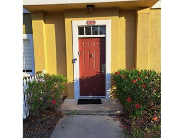 Charming townhome entrance with a red door, white trim, and vibrant red hibiscus bushes at 2618 Lodi Cir # 102, Kissimmee, FL 34746