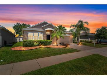 Charming single-story home featuring a well-manicured lawn, tropical landscaping, and brick accents at sunset at 4027 Sunrise Ridge Blvd, Groveland, FL 34736