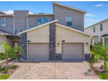 A modern townhome boasts a two-car garage with brick driveway and stone accents, complemented by lush palm trees at 507 Ocean Course Ave # 507, Davenport, FL 33896
