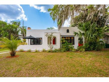 Charming stucco home featuring a red front door, well-manicured lawn, and lush landscaping at 420 N Center St, Eustis, FL 32726