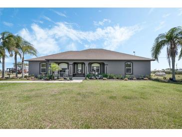 Charming gray home featuring a well-manicured lawn, inviting front porch with rocking chairs, and mature palm trees at 4400 Walker Lake Rd, Bartow, FL 33830