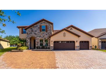 Stunning two-story home with a stone facade, tile roof, three-car garage, and brick driveway at 8625 Brixford St, Orlando, FL 32836