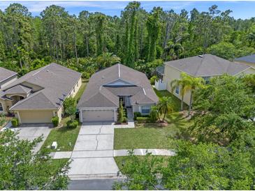 Aerial view of charming single-story home with a two-car garage, well-manicured lawn, and a lush, wooded backdrop at 14750 Hartford Run Dr, Orlando, FL 32828