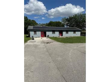 Single story home with a long concrete driveway, solar panels, and red front doors at 434 Diamond Acres Rd, Davenport, FL 33837