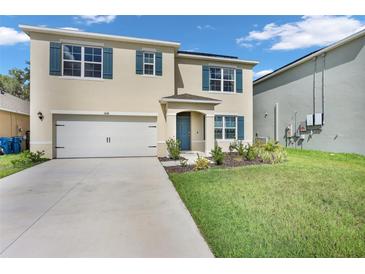 Two-story home with tan stucco, blue shutters, two-car garage, and manicured lawn at 1068 Brooklet Dr, Davenport, FL 33837