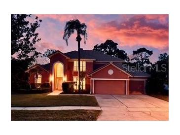 Charming two-story home with a well-manicured lawn, mature trees and a colorful, vibrant sunset in the background at 3020 Zaharias Dr, Orlando, FL 32837