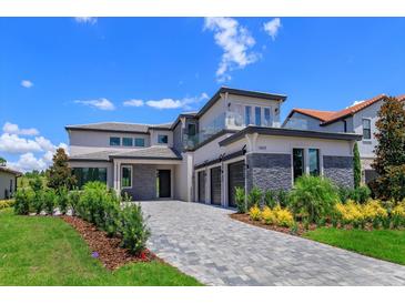 Elegant two-story home with stone accents, a glass balcony, three-car garage, and a paved driveway at 16825 Bolsena Dr, Montverde, FL 34756