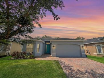 Charming single-story home featuring a brick driveway and a beautifully landscaped front yard under a colorful sunset sky at 3420 Gerber Daisy Ln, Oviedo, FL 32766