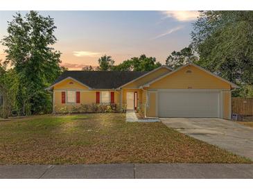 Charming yellow single-story home with a two-car garage, complemented by red shutters and a well-kept lawn at 6906 Colony Oaks Ln, Orlando, FL 32818