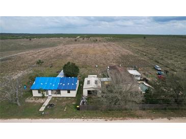 Expansive aerial view of a rural home featuring a blue roof, pool, and outbuildings amidst an open landscape at 270 S Lake Patrick Rd, Frostproof, FL 33843