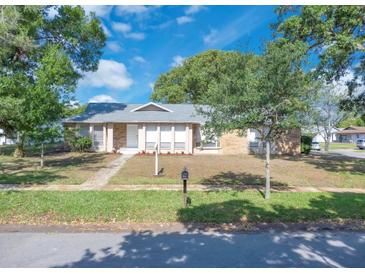 Charming single-story home with a brick facade, well-maintained lawn, and mature trees under a blue sky at 1030 Gran Paseo Dr, Orlando, FL 32825