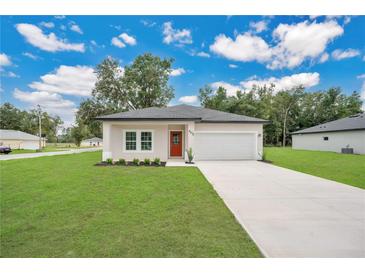 Charming single-story home featuring a two-car garage, a neatly manicured lawn, and a bright, orange front door at 9472 Se 152Nd Pl, Summerfield, FL 34491