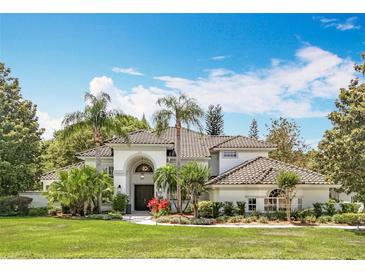 Elegant two-story home featuring a tiled roof, arched entryway, lush landscaping, and a well-manicured lawn at 2540 Hempel Cove Ct, Windermere, FL 34786