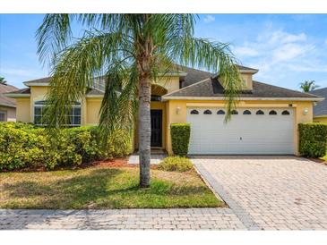 Charming yellow single-story home with a two-car garage, lush landscaping, and a brick paver driveway at 650 Old Bridge Cir, Davenport, FL 33897