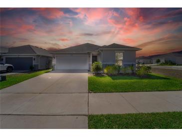 Charming single-story home featuring a two-car garage, well-manicured lawn, and inviting curb appeal under a vibrant sunset sky at 820 Overpool Ave, Davenport, FL 33896