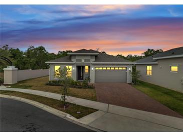 Charming single-Gathering home showcasing a well-manicured lawn, brick driveway, and modern architectural details at sunset at 7651 Five Oaks Dr, Harmony, FL 34773