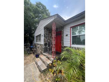 Charming home featuring a stone facade, red door, and decorative support beams at 7506 Mott Ave, Orlando, FL 32810