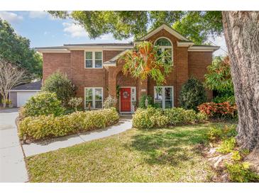 Charming brick home featuring a red front door, lush landscaping, and mature trees at 343 Raleigh Pl, Oviedo, FL 32765
