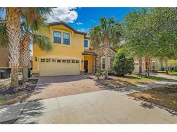 Two-story home with a two-car garage, brick driveway, stone accents, and lush landscaping with palm trees at 8804 Rhodes Street, Kissimmee, FL 34747