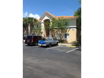 Tan condo building featuring a tile roof, palm trees, and parking in front at 495 Las Cortes Ln # 206, Orlando, FL 32824