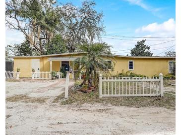 Charming single-story home with yellow exterior, white picket fence and mature trees at 5501 Vance Ave, Orlando, FL 32810