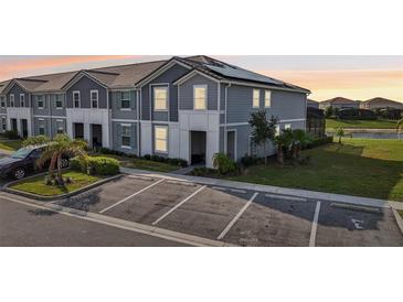 Two-story townhome featuring a gray exterior, solar panels, landscaping, and convenient parking spaces at 7554 Oak Spring Ln, Davenport, FL 33837