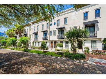 Charming townhome showcases a white facade, manicured landscaping, and a welcoming brick-paved street at 220 S Summerlin Ave, Orlando, FL 32801
