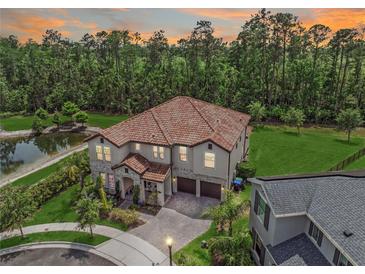 Stunning aerial view of a two-story home with a tile roof, lush landscaping, and a serene pond at 8478 Elba Isle Ct, Windermere, FL 34786