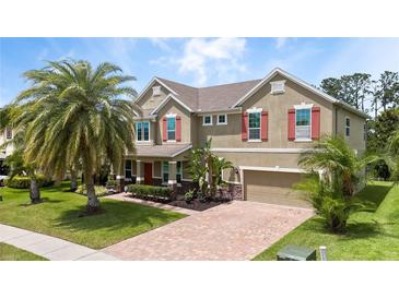 Charming two-story home with a brick driveway, beautiful landscaping, and a large palm tree at 15242 Heron Hideaway Cir, Winter Garden, FL 34787