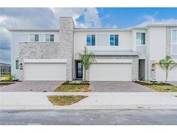New townhouse exterior shows modern architecture with brick driveway, stone accents, attached garage and tasteful landscaping at 502 Bogey Dr, Davenport, FL 33896
