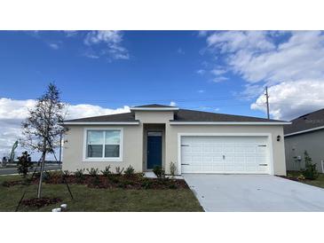 Charming single-Gathering home with a two-car garage, blue entry door, and beautifully landscaped front yard at 1012 Bear Hammock Dr, Umatilla, FL 32784