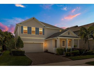 Charming two-story home with a manicured lawn and inviting brick driveway at dusk at 14742 Bahama Swallow Blvd, Winter Garden, FL 34787
