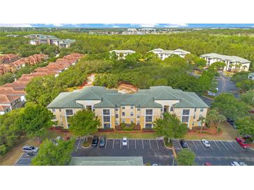 An aerial view of an apartment complex with a green roof and ample parking nestled in a lush, green landscape at 8908 Legacy Ct # 303, Kissimmee, FL 34747