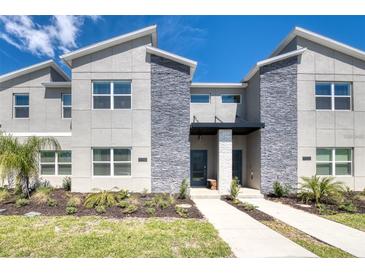 Modern townhouse with stone accents, manicured landscaping, and a welcoming entrance under a bright blue sky at 8993 Cabot Cliffs Dr, Davenport, FL 33896