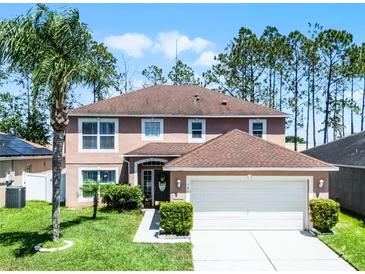 Charming two-story home featuring a well-manicured lawn, a two-car garage, and lush tropical landscaping at 140 Elgin Blvd, Davenport, FL 33897