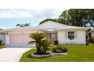 Charming single-story home with well-manicured lawn, lovely shrubbery, and a pink accent on the shutters and garage door at 32900 Crooked Oaks Ln, Leesburg, FL 34748