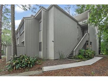 Exterior view of a gray two-story home featuring wood siding, stairs to the front door, and lush landscaping at 111 Crown Oaks Way # 101, Longwood, FL 32779