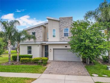 Contemporary two-story home with stone accents, paver driveway, and lush tropical landscaping at 303 Ocean Course Ave, Davenport, FL 33896