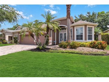 Beautifully landscaped single-Gathering home featuring a brick driveway and lush green lawn, with palm trees and colorful flower beds at 453 Kays Landing Dr, Sanford, FL 32771