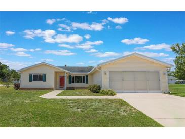 Charming single-story home featuring a well-maintained lawn, red front door, and two-car garage at 10980 Sw 62Nd Ave, Ocala, FL 34476