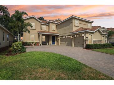 Beautiful two-story home with a three-car garage, brick driveway, and vibrant landscaping under a stunning colorful sunset sky at 1082 Trappers Trail Loop, Davenport, FL 33896