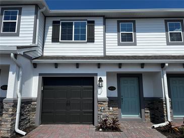 Charming townhouse showcasing a gray garage door, a light blue front door, and stone accents on the lower portion of the facade at 5113 Prairie Preserve Run, St Cloud, FL 34772