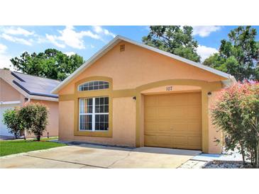 Charming one-story home with tan stucco, arched window, tan garage door, and manicured landscaping at 107 Pamala Ct, Sanford, FL 32771