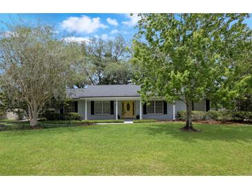 Charming single-story home featuring a manicured lawn, mature trees, and a welcoming yellow front door at 1204 Howell Creek Dr, Winter Springs, FL 32708