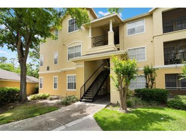 Inviting yellow condo building featuring well-kept landscaping, a stairway, and balcony, all set against a blue sky and green trees at 2652 Robert Trend Jones # 2652, Orlando, FL 32835