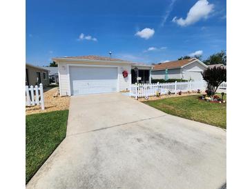 Charming single-story home featuring a well-manicured lawn, white picket fence, and attached garage at 16922 Se 81St Charlesfort Ave, The Villages, FL 32162