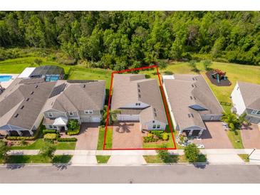Aerial view of a single-Gathering home with a manicured lawn and brick driveway, surrounded by lush trees at 11054 Cyrilla Woods Dr, Orlando, FL 32832
