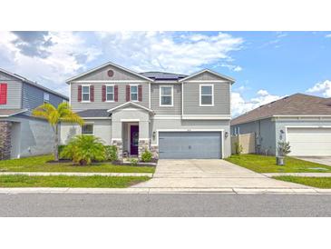 Two-story home with gray siding, stone accents, two car garage, and well-maintained landscaping at 1631 Pontiff Pl, Davenport, FL 33896